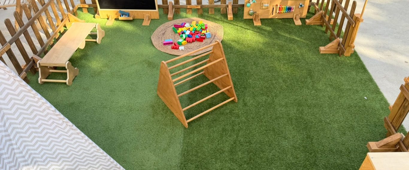 Depatitos: un espacio para explorar y jugar Espacio Depatitos con tipi, triángulo de escalada, banco de equilibrio, construcciones y panel sensorial dentro de un recinto de madera.